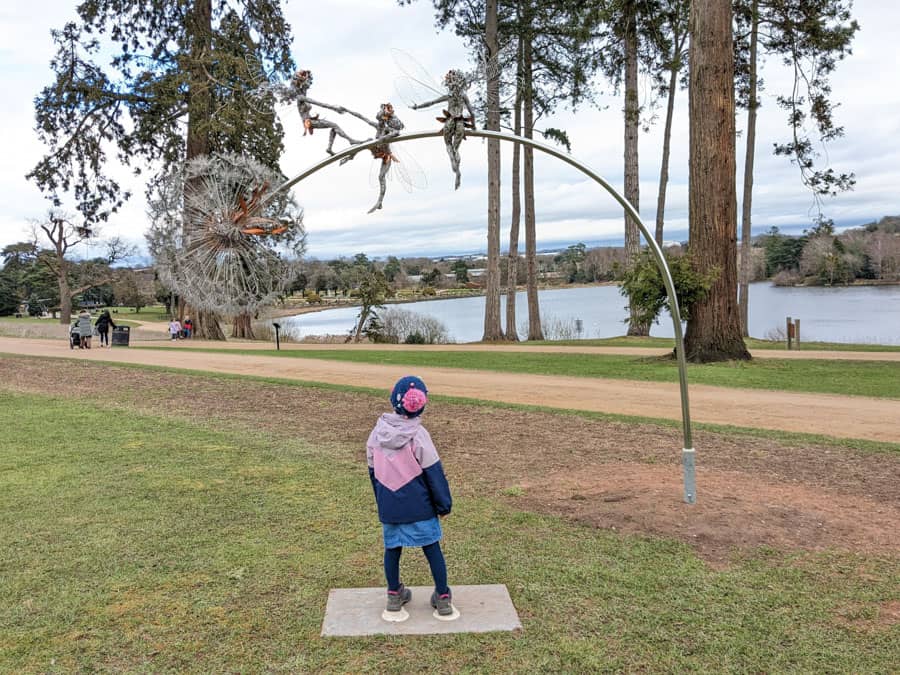 Child looking up at a wire sculpture of fairies by a lake