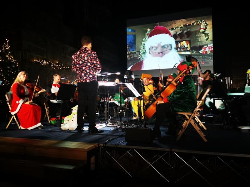 Santa on a big screen with an orchestra in front