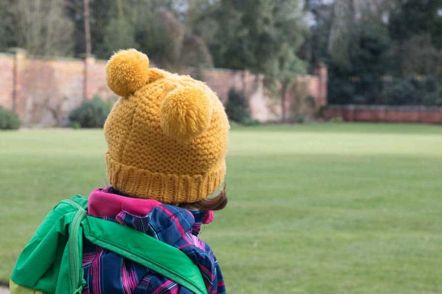 Child in yellow bobble hat looking into walled garden