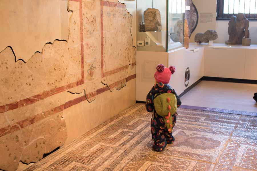 Toddler with dinosaur backpack on mosaic floor
