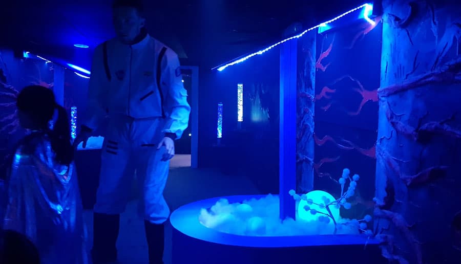 Dark, blue room with a man dressed as a space ranger and glowing large eggs