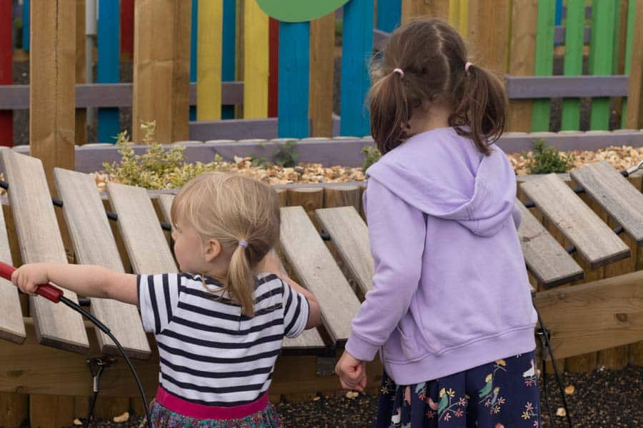 Two children playing a large wooden xylophone