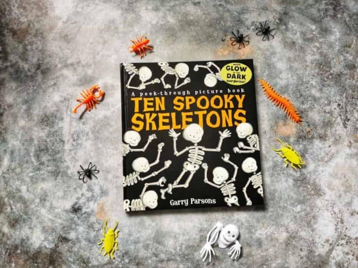 Ten spooky skeletons book on a grey background surrounded by halloween plastic creatures