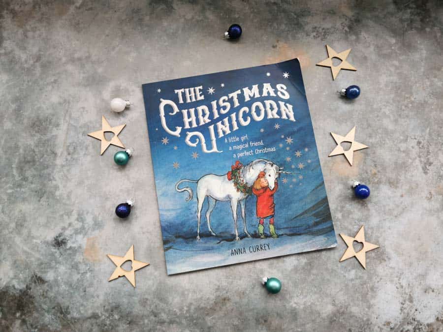 Copy of the Christmas unicorn, childrens book on a stone background with mini christmas decorations surrounding it