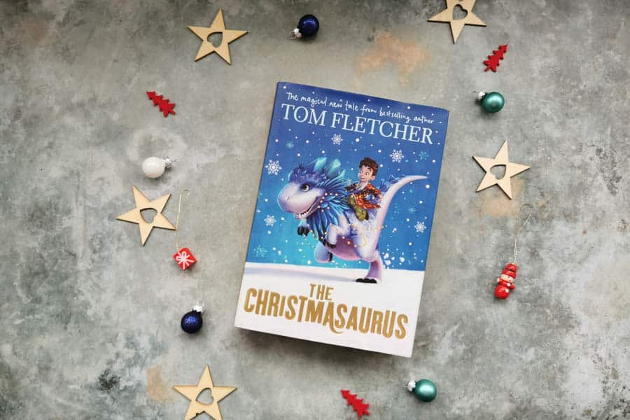 Copy of the Christmasaurus, childrens book on a stone background with mini christmas decorations surrounding it