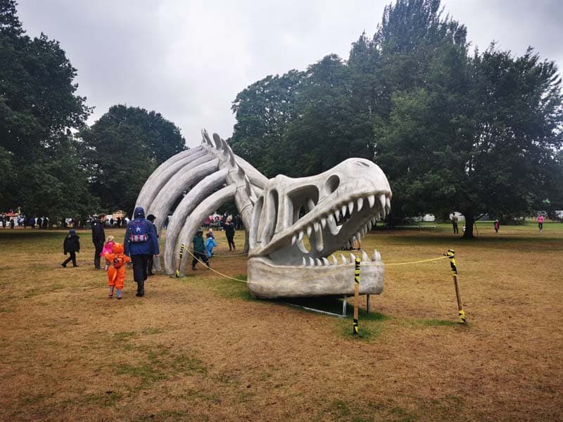 Large dinosaur skeleton in a field surrounded by families