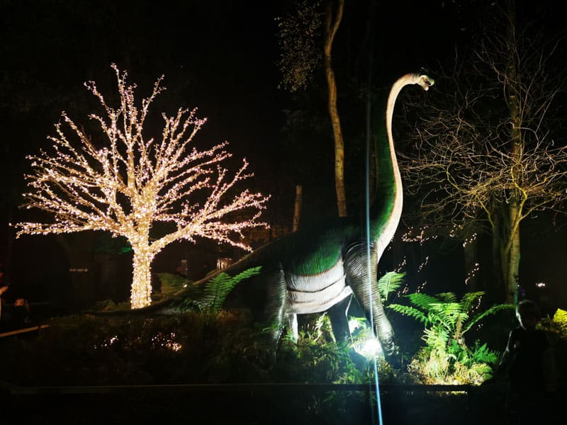 Dinosaur sculpture at night and lit up tree