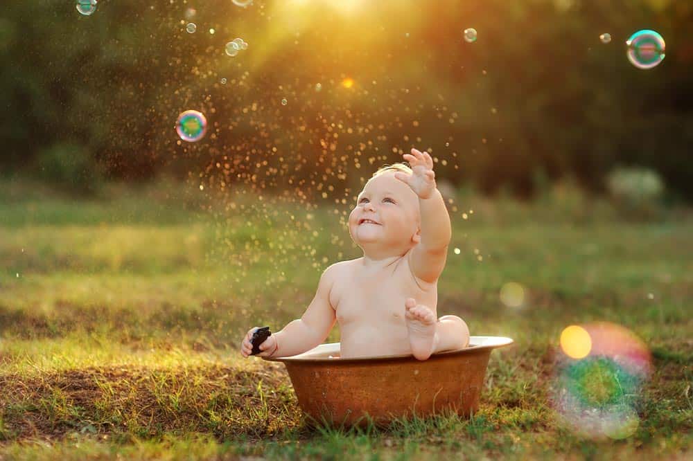 Baby in a bowl on the grass surrounded by bubbles in the air