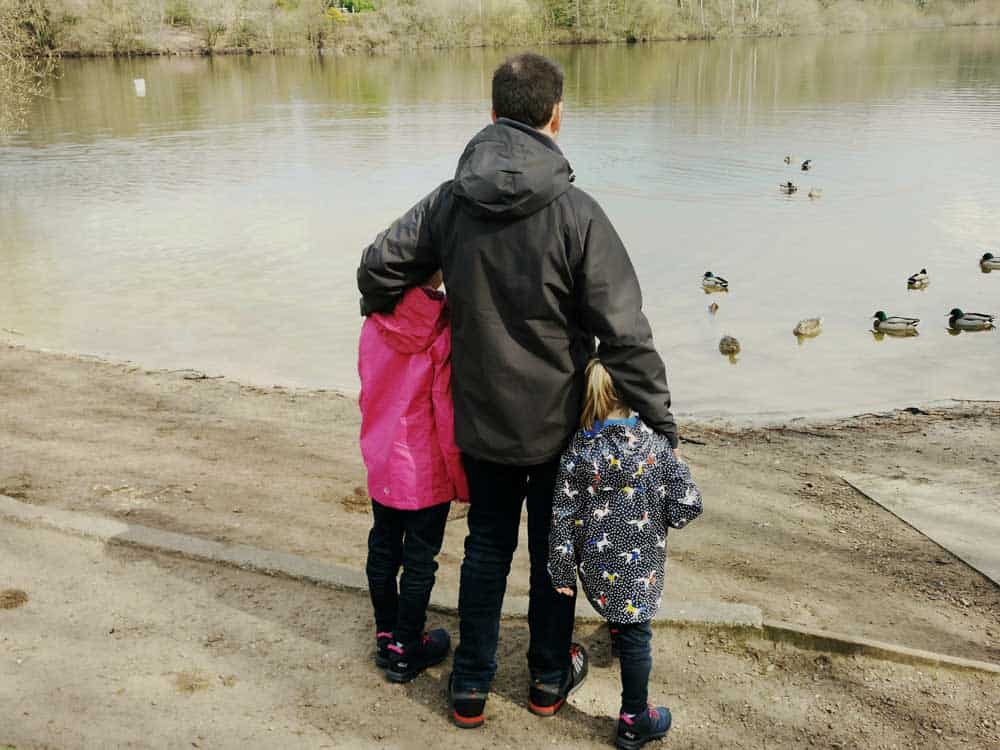 Father and daughters by a duck pond