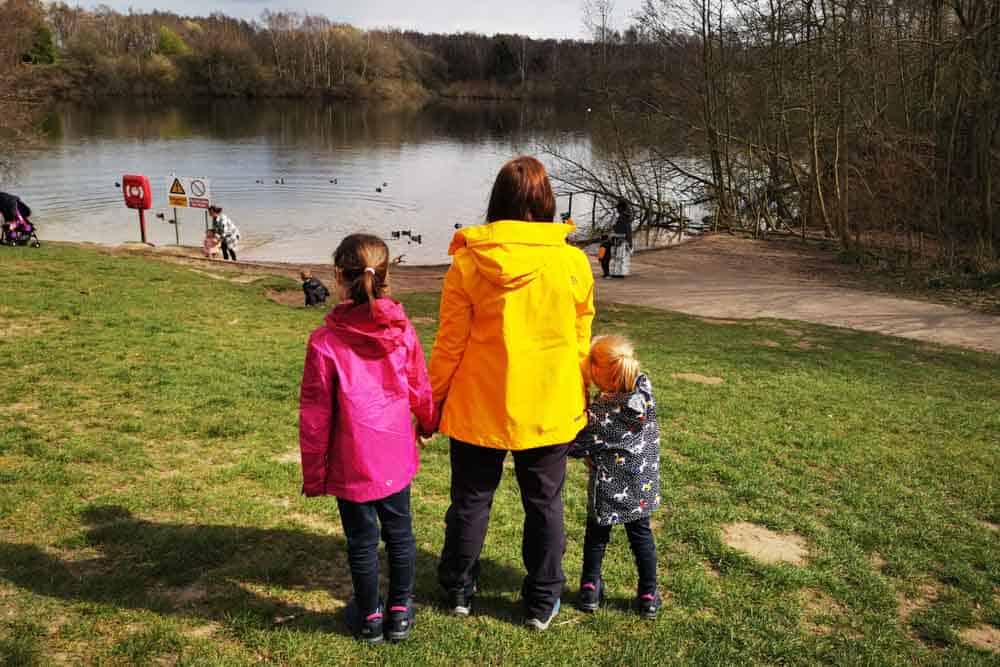 mum and two girls in raincoats looking out over duck pond