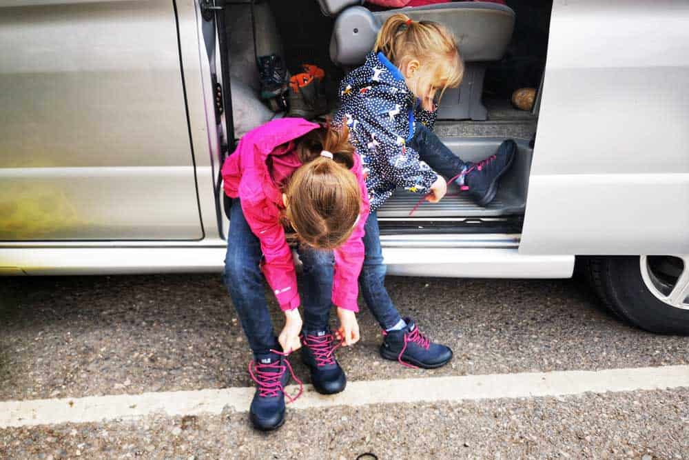 Two children sat on campervan steps putting on walking shoes