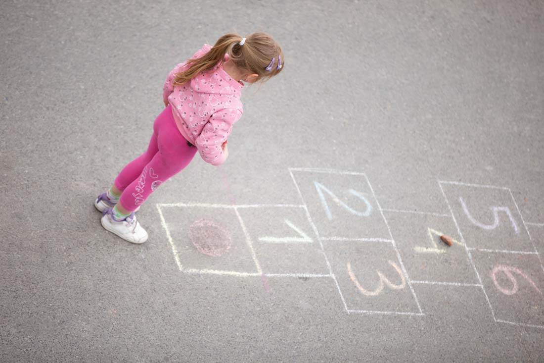 Girl stood next to a hopscotch board drawn on the floor