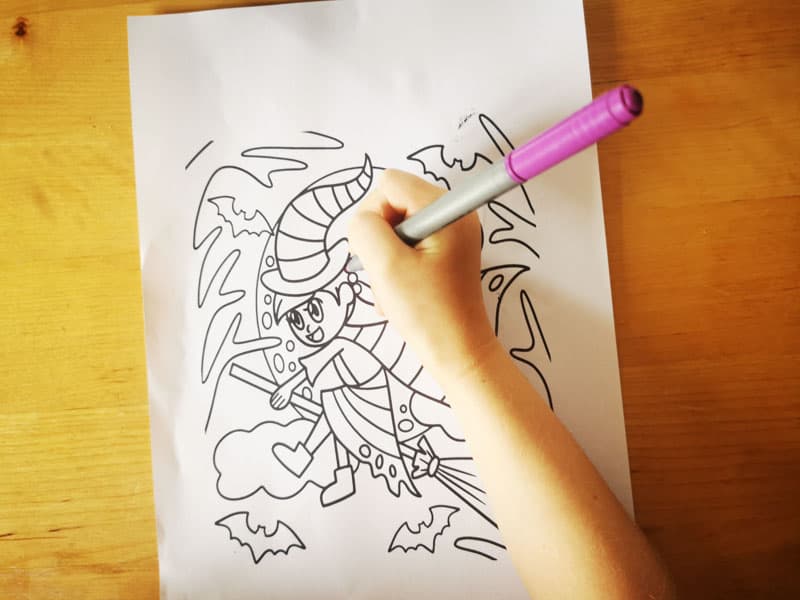 Childs hand colouring a line drawing of a witch