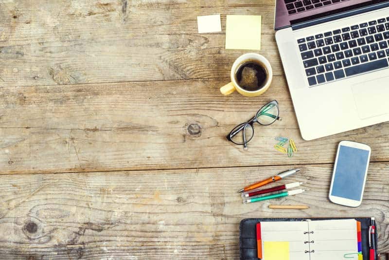 Wooden desk with laptop and pens, notebook, coffee etc