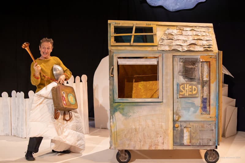 Man on stage by little hut on wheels