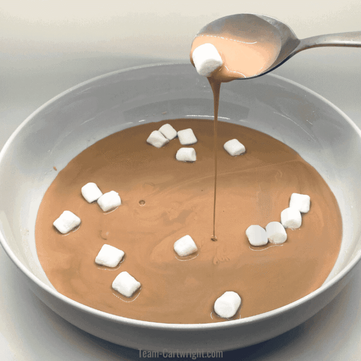 bowl of brown liquid with a spoon lifting out mini marshmallows