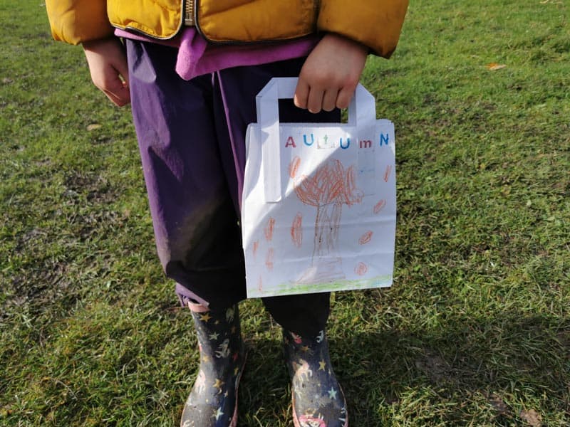 child holding a paper bag with drawings on it. Dressed for autumn, in a field