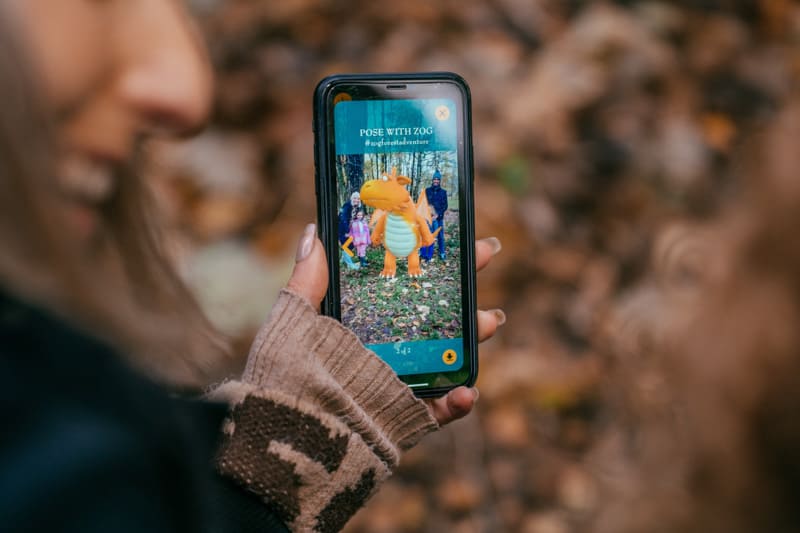 Phone held up in a forest with photo of a family with Zog
