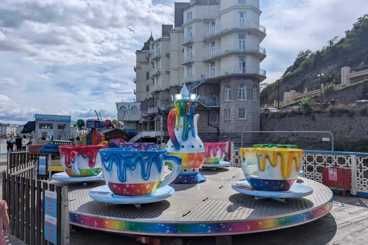 Colourful teacup amusement ride on Llandudno seafront with oversized painted cups and a central teapot surrounded by Victorian style buildings. The family attraction sits beside the promenade under a cloudy sky, showcasing one of the town’s traditional seaside amusements.