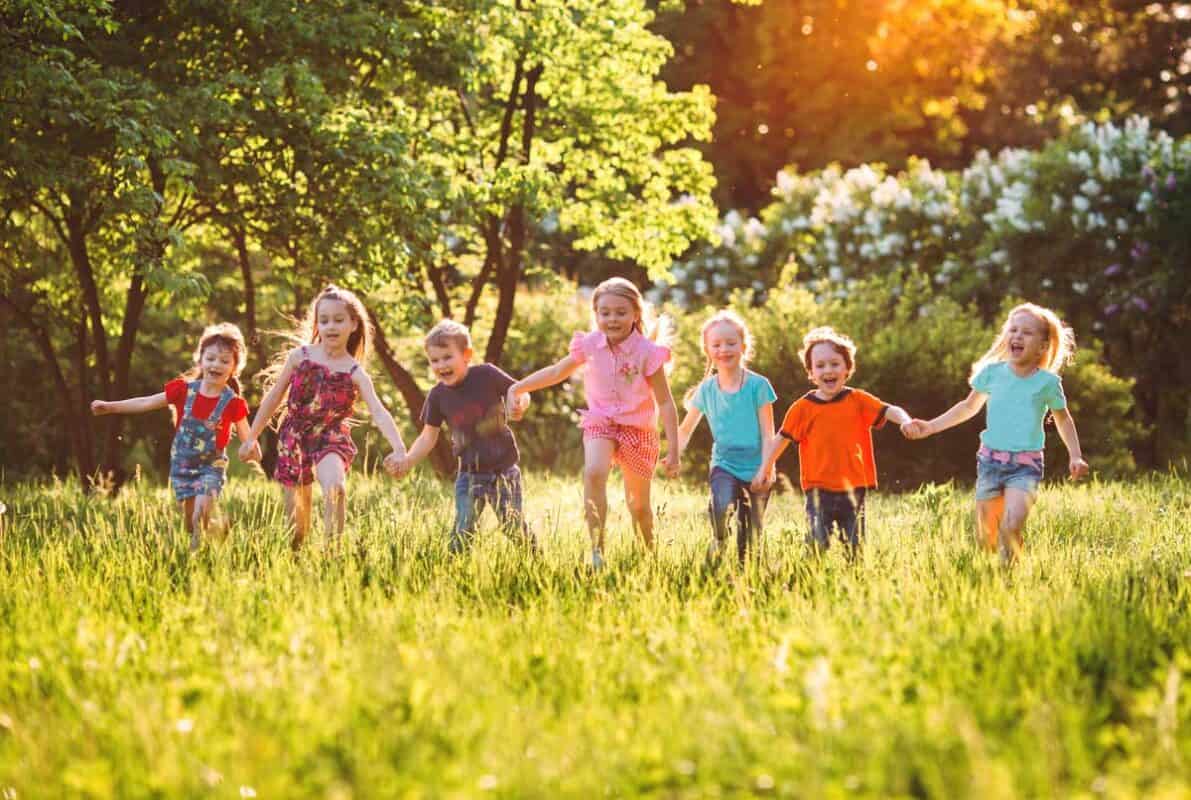 Large group of kids, friends boys and girls running in the park on sunny summer day in casual clothes
