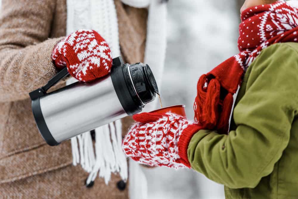 Hot chocolate flask and two gloved hands pouring it