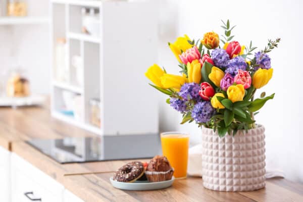 Vase of flowers on a table with orange juie and baked goods