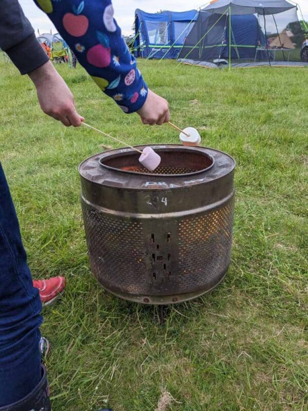 Metal fire pit with two hands holding sticks with marshmallows on the end