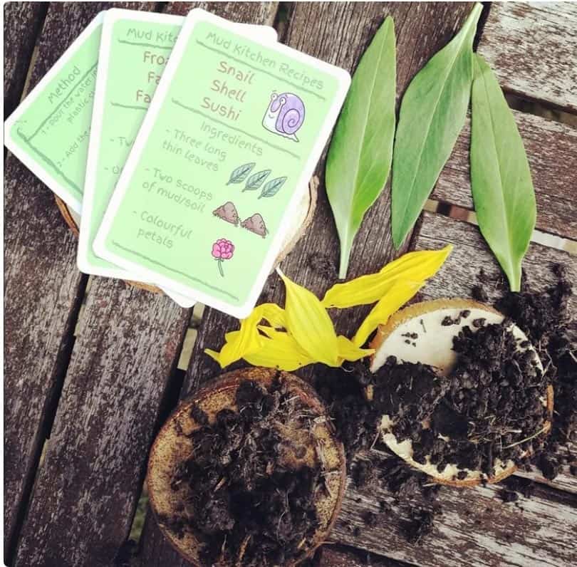 Some green gards with mud kitchen recipes on them. On a wooden table top with mud pies