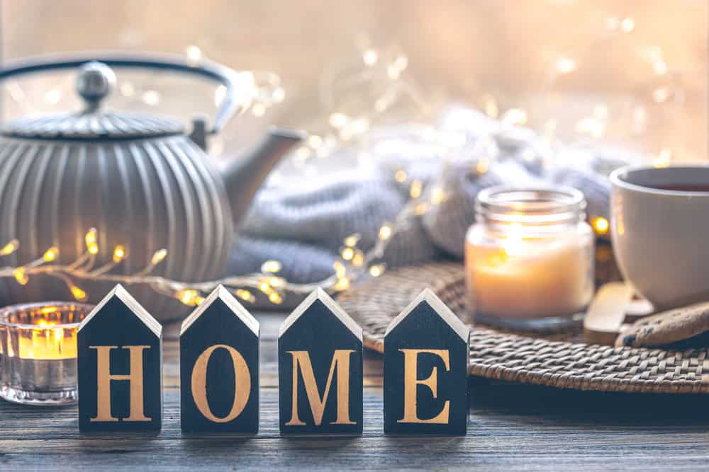 Cosy image of kettle, fairy lights, candle and home sign