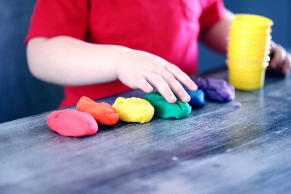 Childs hand in a red t-shirt with a row of colourful balls of play doh