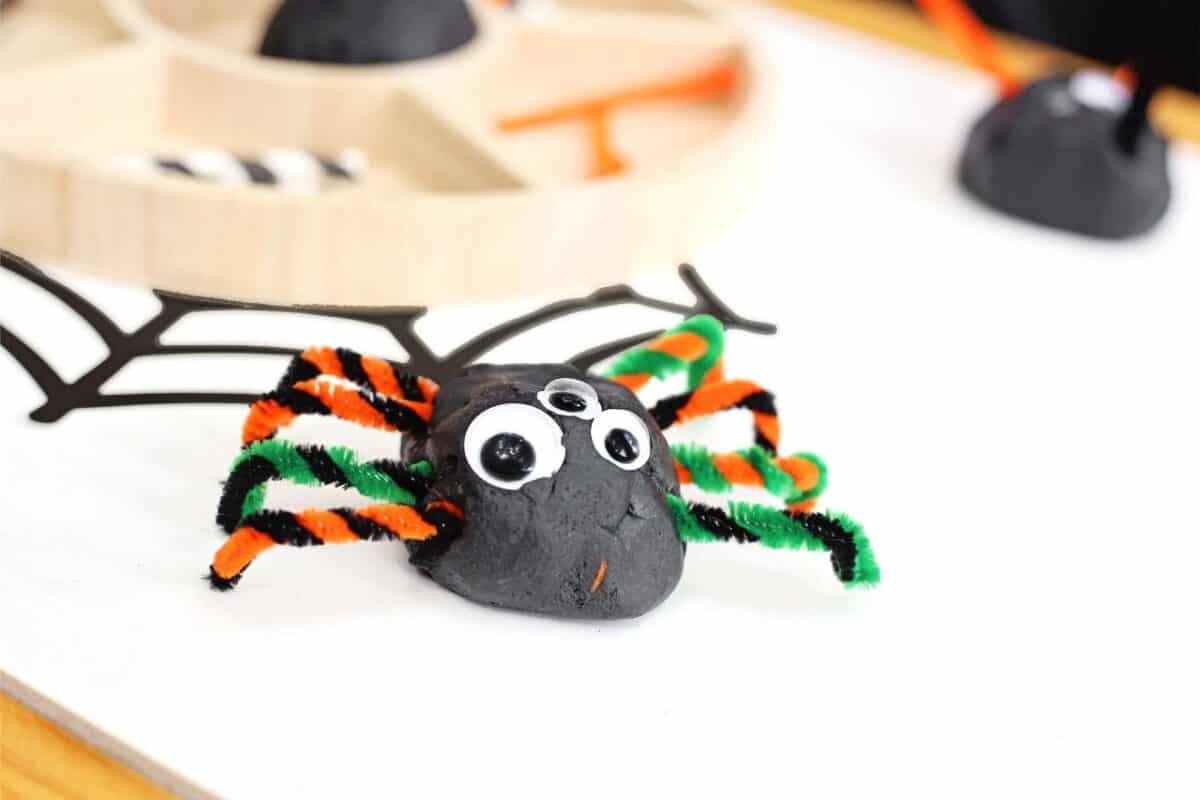 Black ball of playdough with googly eyes and pipe cleaner legs
