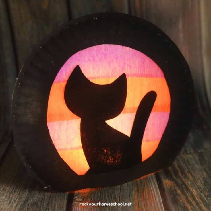 Halloween paper craft featuring a black cat silhouette against a glowing orange and purple tissue paper background