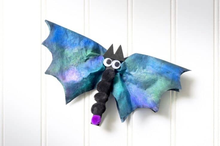 Halloween bat craft made from a painted coffee filter for wings, black pom-poms for the body, googly eyes, and a purple nose.