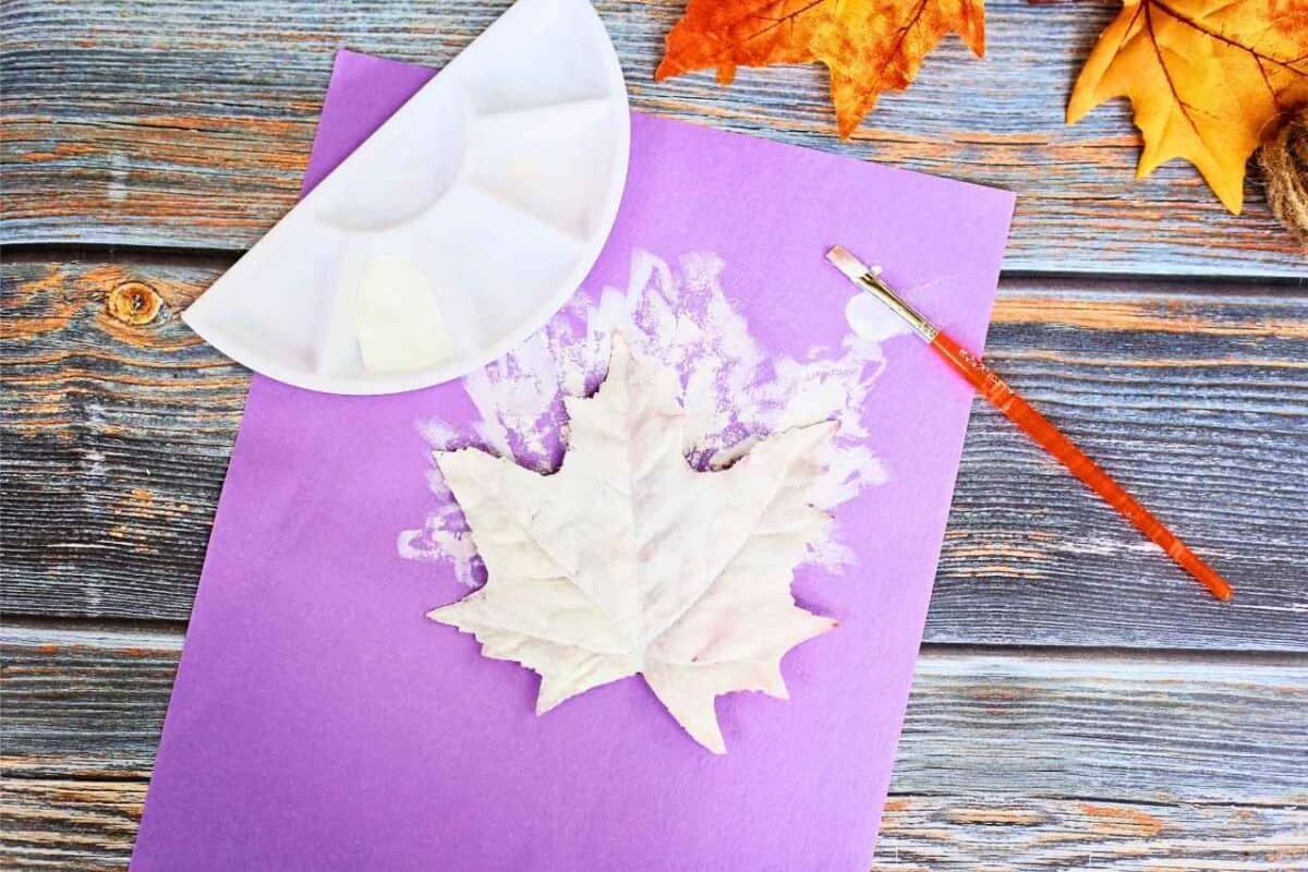 Purple sheet of paper with a leaf on top that has been painted white