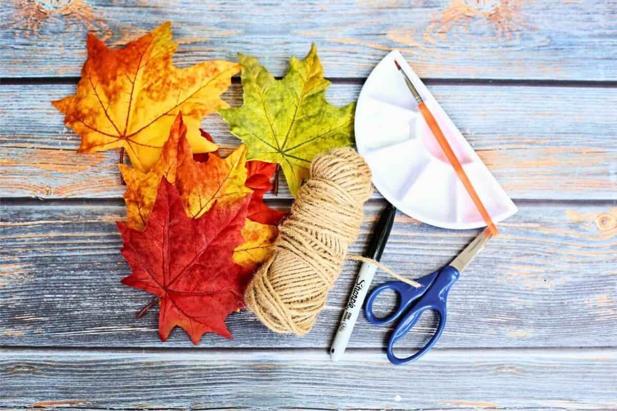 pile of leaves, roll of twine, black pen, scissors  and paint pallet and brush on a wooden background