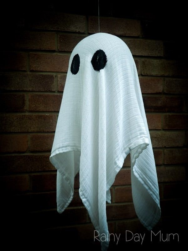 Homemade Halloween decoration of a floating ghost made from a white cloth with black eyes, hanging in front of a brick wall.