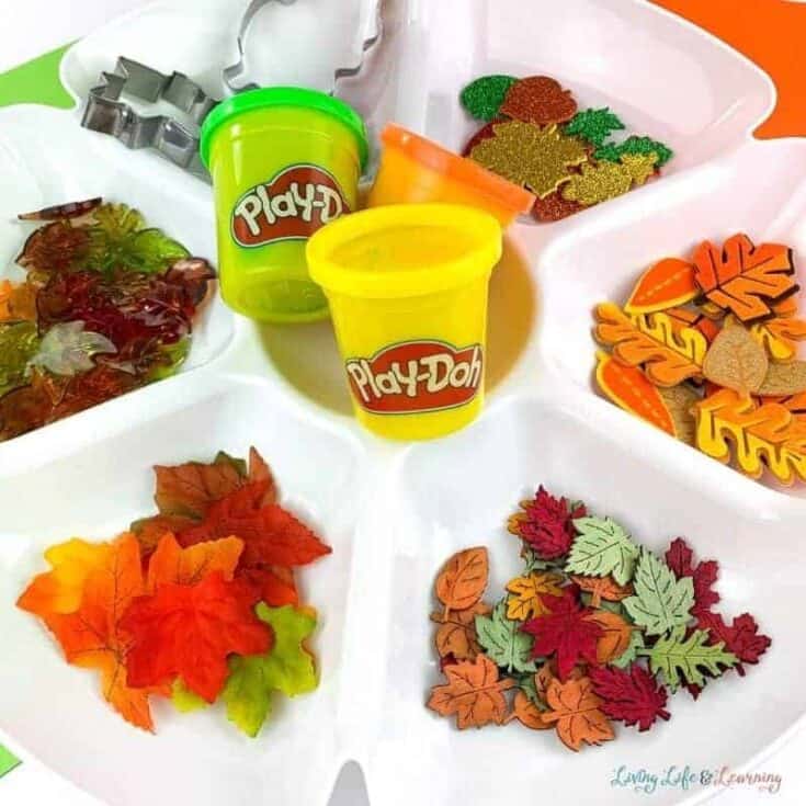 Brown playdough with leaf-shaped cutouts stamped using a red plastic leaf stamp on a white surface.