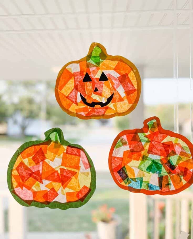 Pumpkin suncatcher crafts made from colorful tissue paper pieces, with one shaped as a jack-o’-lantern face, hanging on a window