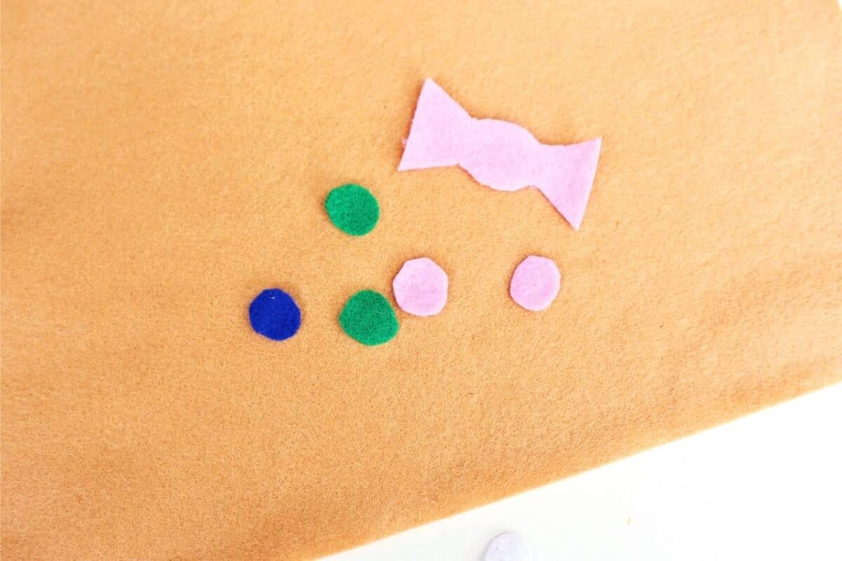 Small felt cut-outs including a pink bow and colourful circles placed on a tan felt background