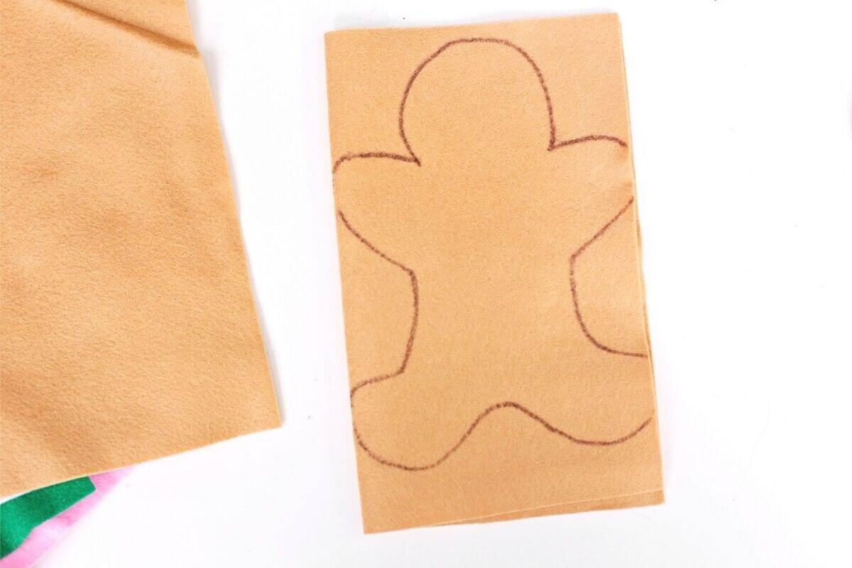 Outline of a gingerbread person drawn on folded tan felt ready to be cut out.