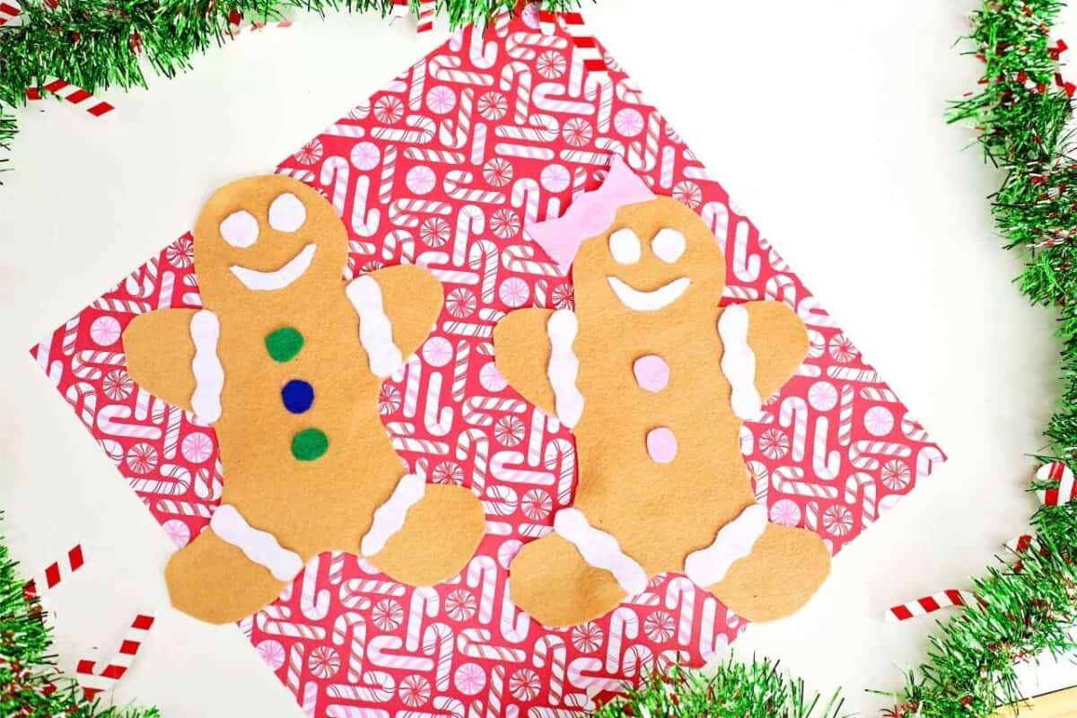 Two decorated felt gingerbread people with icing, buttons and a bow displayed on red candy cane patterned paper with tinsel
