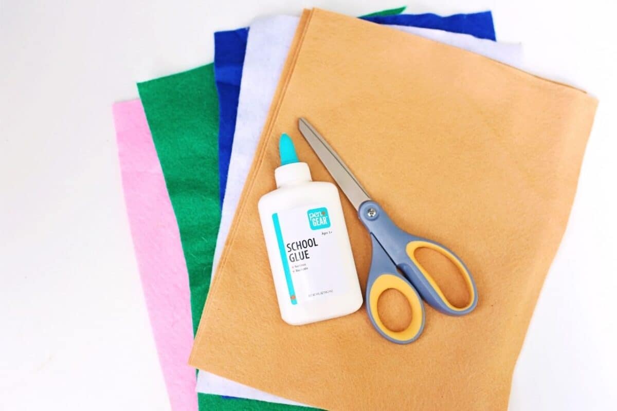Craft supplies for felt gingerbread people including coloured felt sheets, scissors, and a bottle of school glue.