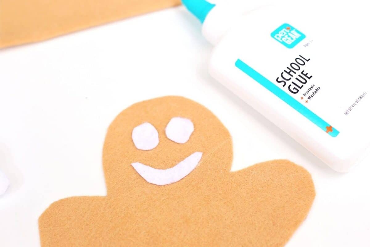 Felt gingerbread person with white felt eyes and smile being glued in place next to a bottle of school glue