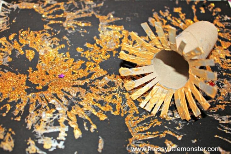 Toilet paper roll fireworks craft showing gold glitter paint bursts on black paper made by stamping with a cut cardboard tube