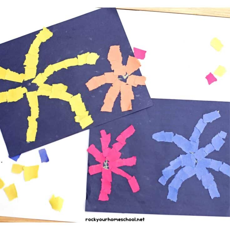 Torn paper fireworks craft made by kids using bright yellow, orange, pink, and blue paper pieces arranged on dark card to create firework shapes.