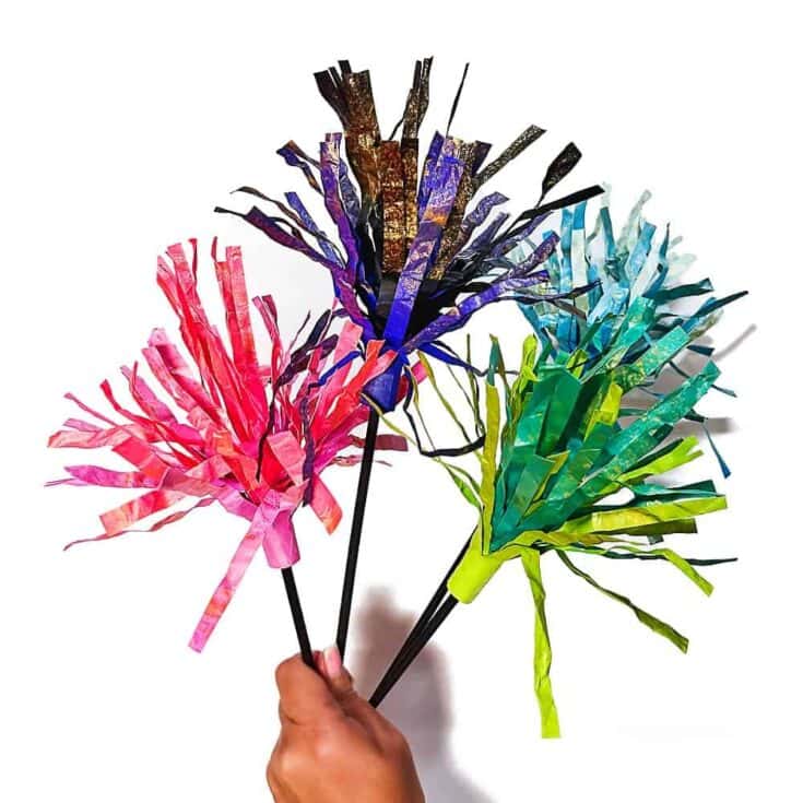Child holding colourful DIY paper sparklers made from rolled paper and tissue strips in pink, purple, blue, and green to resemble fireworks