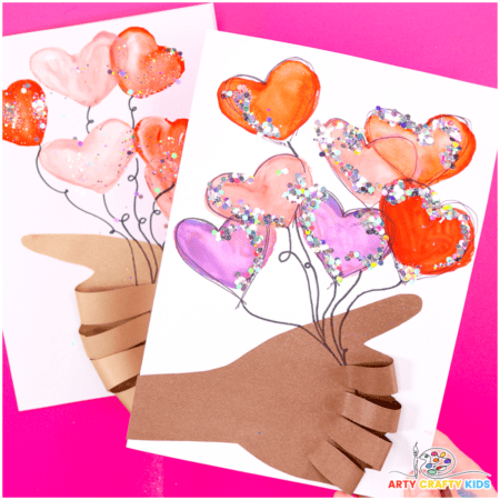 Two handmade Valentine’s cards feature brown paper cutouts of hands holding heart-shaped balloons painted in shades of red, pink, and purple. The hearts are outlined in glitter and connected to the hands with drawn string lines, creating a bouquet effect against a white background.
