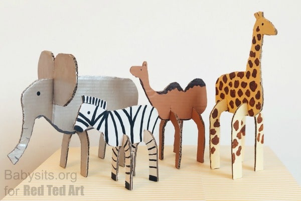 Cardboard cutout safari animals. An elephant zebra camel and giraffe stand upright on a light surface in a simple handmade craft display.