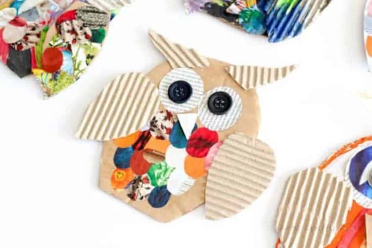 Brown owl craft made from cut cardboard with striped corrugated wings, pointed ears, and large black button eyes on a white background. The owl belly is decorated with colorful paper circles, and parts of other handmade owl crafts appear around the edges.