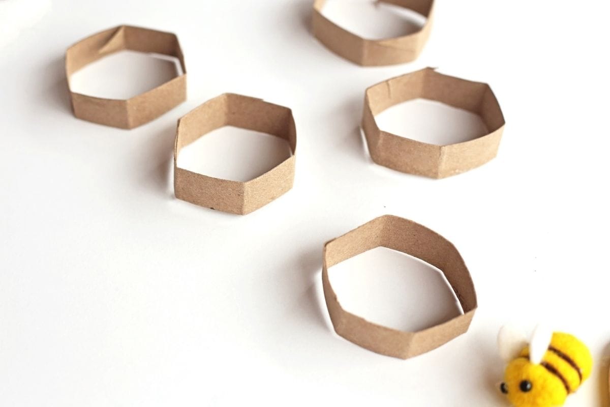 Cardboard strips folded into small hexagon shapes are arranged on a white surface to create honeycomb pieces for a bee sensory bin activity.